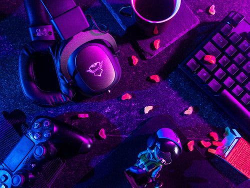 A colorful and abstract composition featuring various gaming and technology-related objects such as a gaming headset, Xbox controllers, keyboard and other electronic devices in a dark, neon-lit environment
